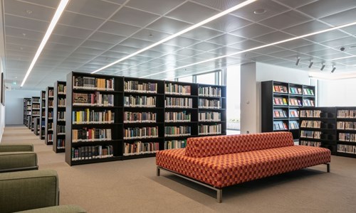 two green sofas on the left , one checkered orange and red double-sided sofa and a stack of library books behind it and another stack on the right hand side (a library photo from AKC)