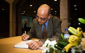 A man in grey suit sitting and signing a book