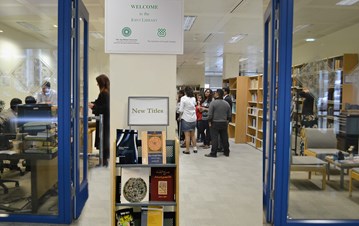 A photo from the library entrance with books in the front, books on the right hand side and group of people listening to someone