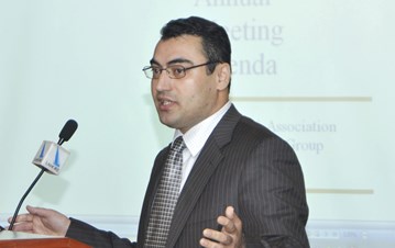 A side view of a man in suit speaking over a podium with a presentation in the background