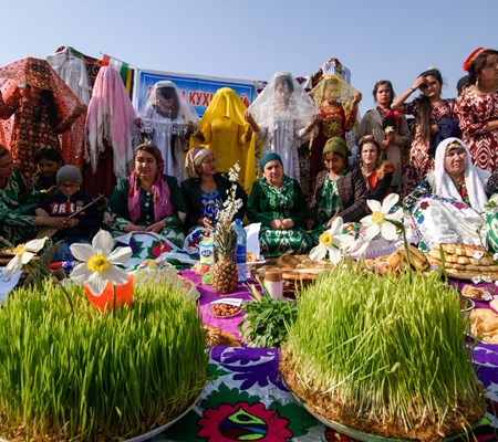 Tajiki Ismailis celebrating and posing for a picture in local dresses during their cultural festival in a group with food items in the front 