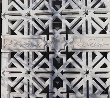 An image of geometric patterns carved in a grill with Arabic inscriptions written between them